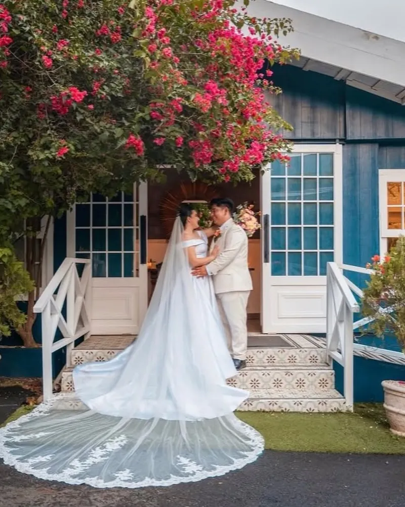 Novios en la entrada de la casa azul, con el velo extendido sobre el zacate y buganvilias encima
