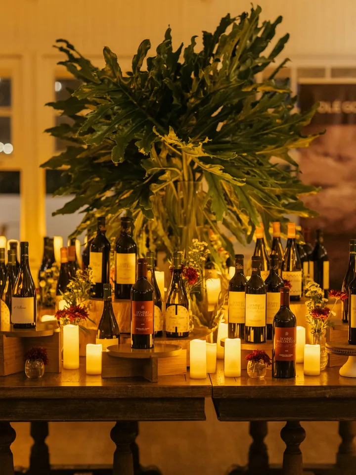 Mesa con botellas de vino, velas encendidas y un arreglo de hojas verdes
