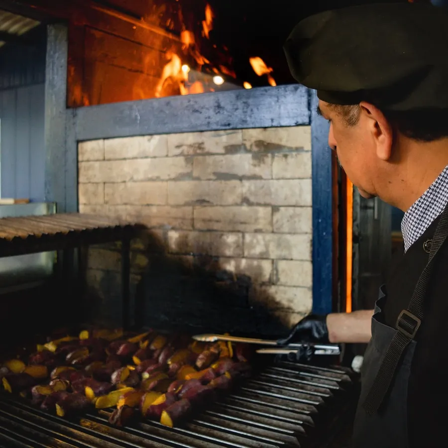 Parrillero frente al fuego de la parrilla, con brochetas de carne sobre las brasas