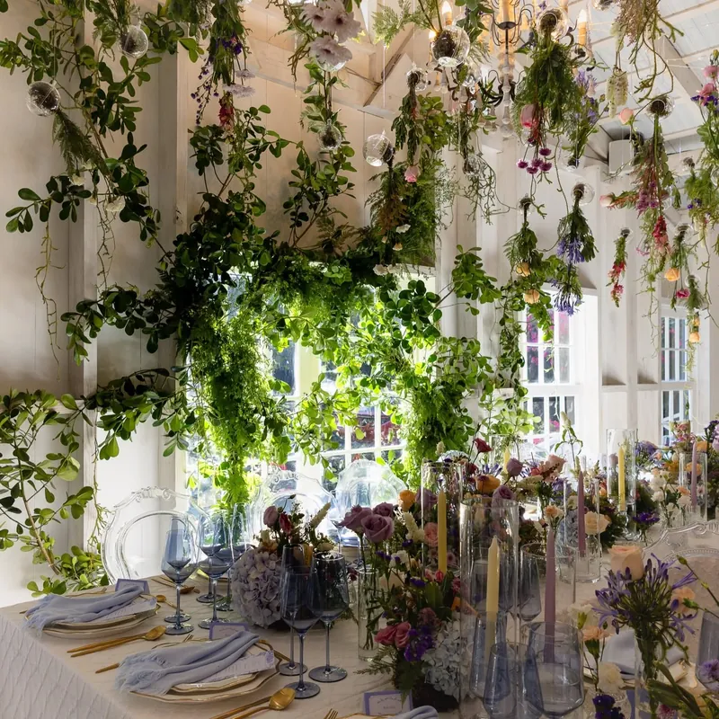 Flores y enredaderas colgando del techo sobre una mesa larga con copas