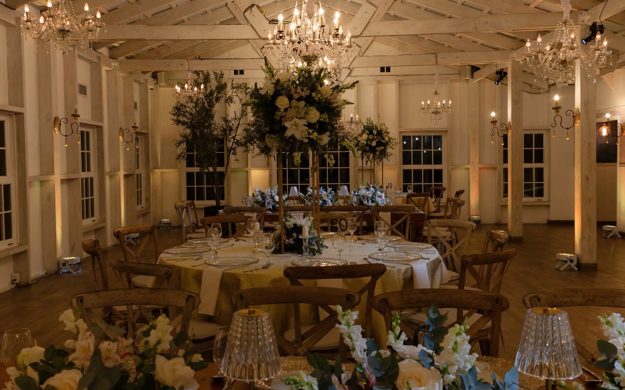 El salón de Estancia Novillo montado para una boda, con vigas blancas de madera, candelabros de cristal y mesas con flores