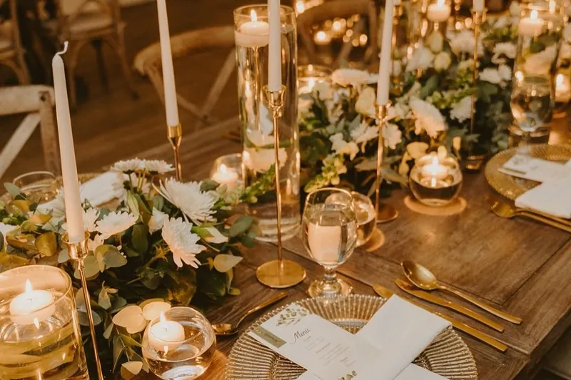 Detalle de una mesa con velas flotantes, flores blancas y cubiertos dorados