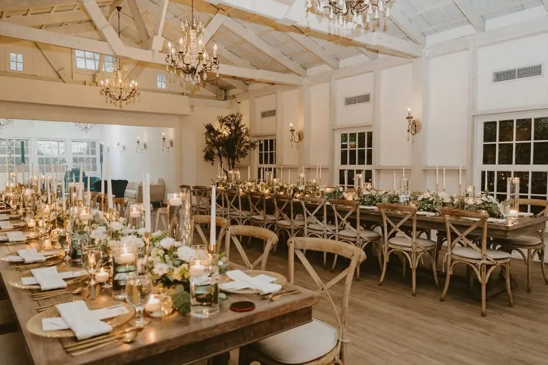 Mesas largas de madera con velas y flores blancas dentro del salón