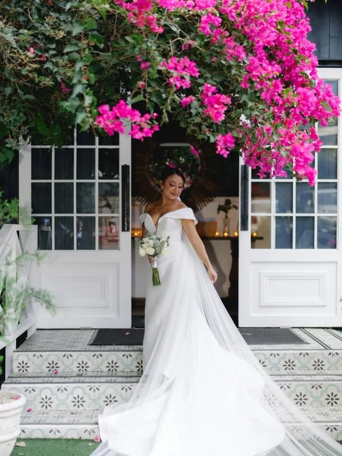 Novia en la puerta de la casa, entre buganvilias fucsia y el piso de mosaico