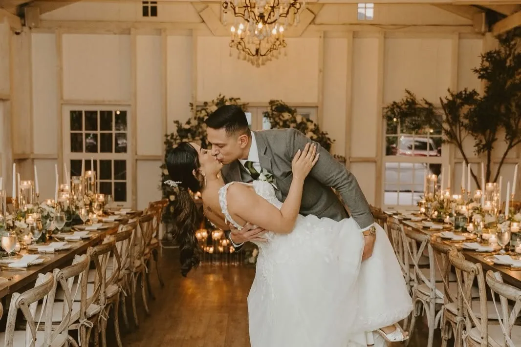 Novios bailando en el salón entre mesas largas con velas