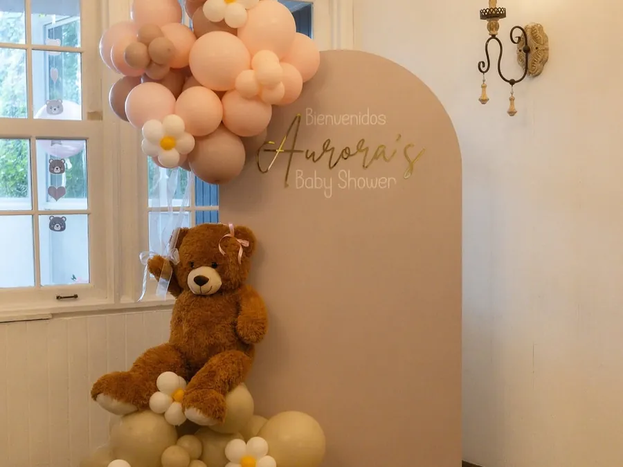 Rincón de un baby shower con un oso de peluche sobre globos color arena