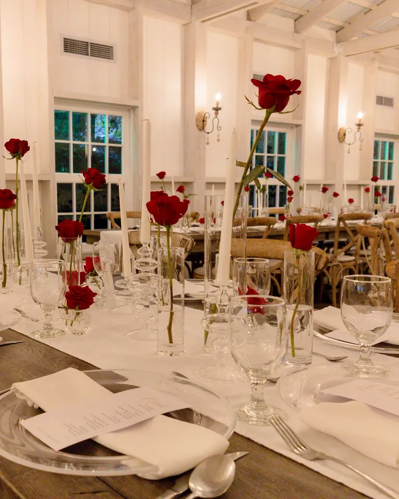 Mesas con manteles blancos y rosas rojas en floreros altos
