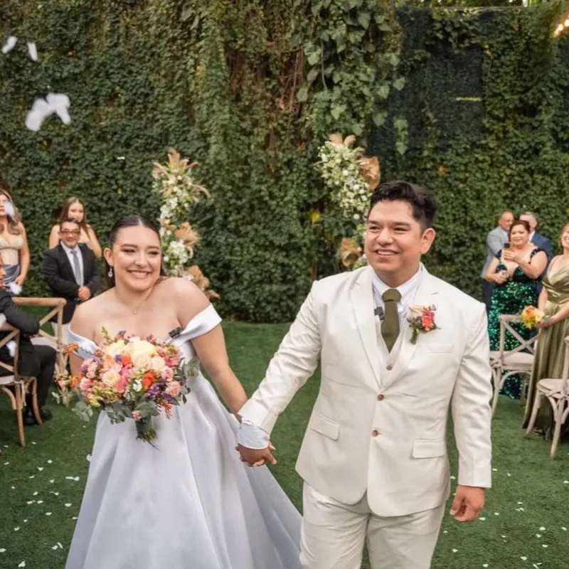 Novios saliendo de la ceremonia en el jardín, tomados de la mano y sonriendo