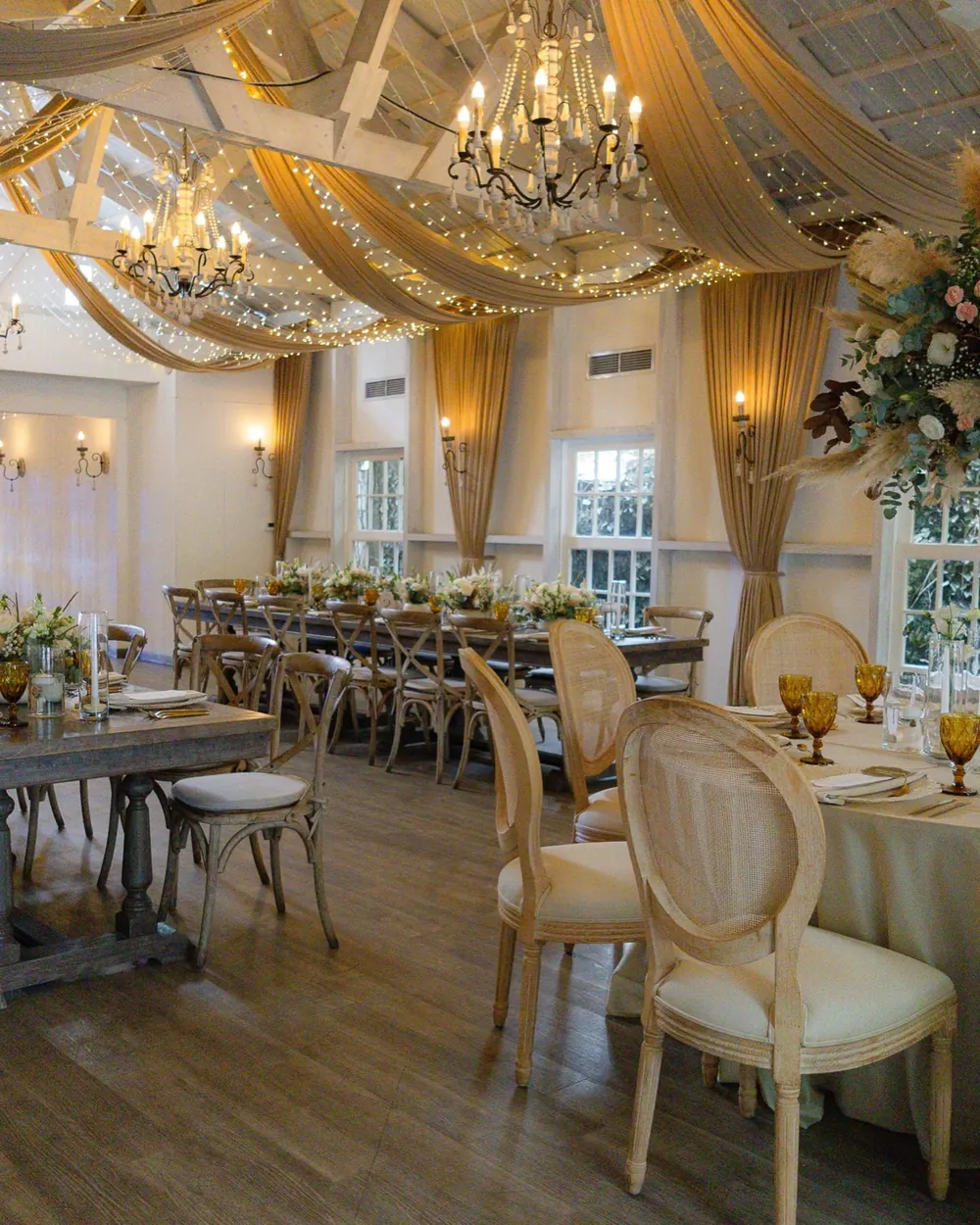 Salón principal con cortinas doradas, luces colgantes, candelabros y mesas largas de madera